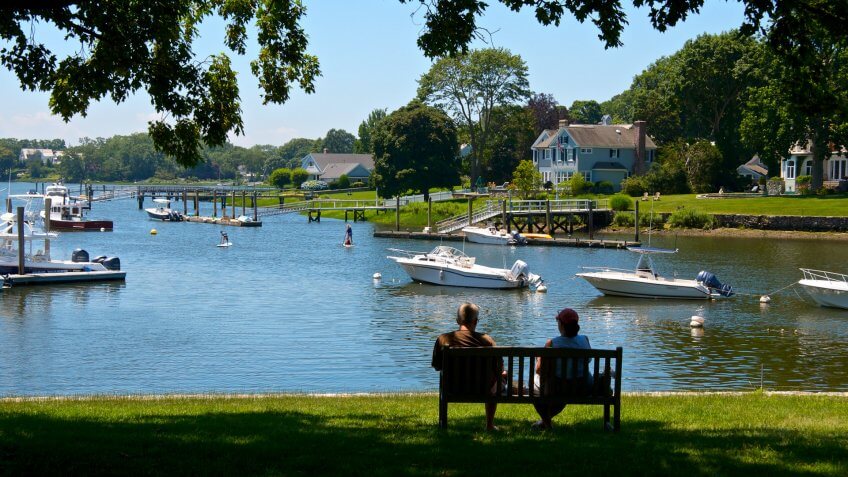 Connecticut, USA - July 05, 2013: A couple sit on a bench in cool shade at the shoreline of a Long Island Sound inlet in summer time, Rowayton, Connecticut, New England.