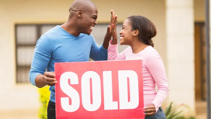 cheerful young african couple holding sold sign and celebrating their house been sold.