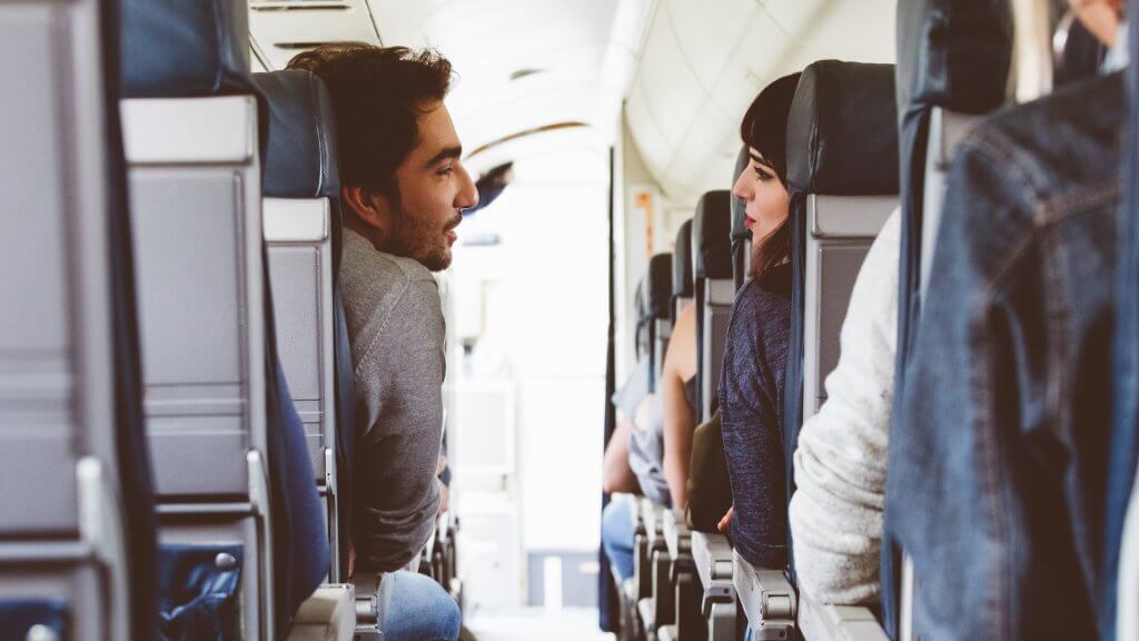 people sitting in airplane seats talking across the aisle