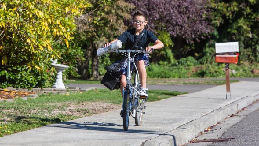A young boy delivering newspapers on his bicycle.