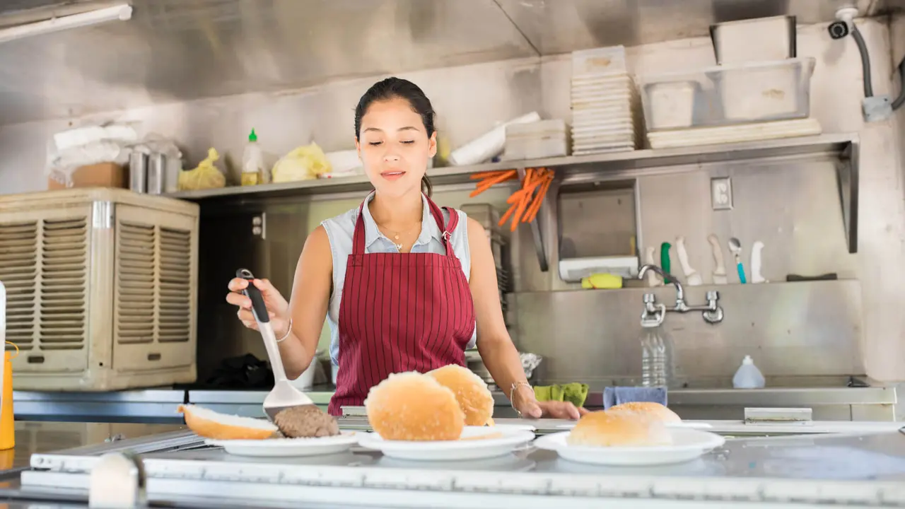 Attractive young woman with an apron working in a food truck and preparing a few burgers.