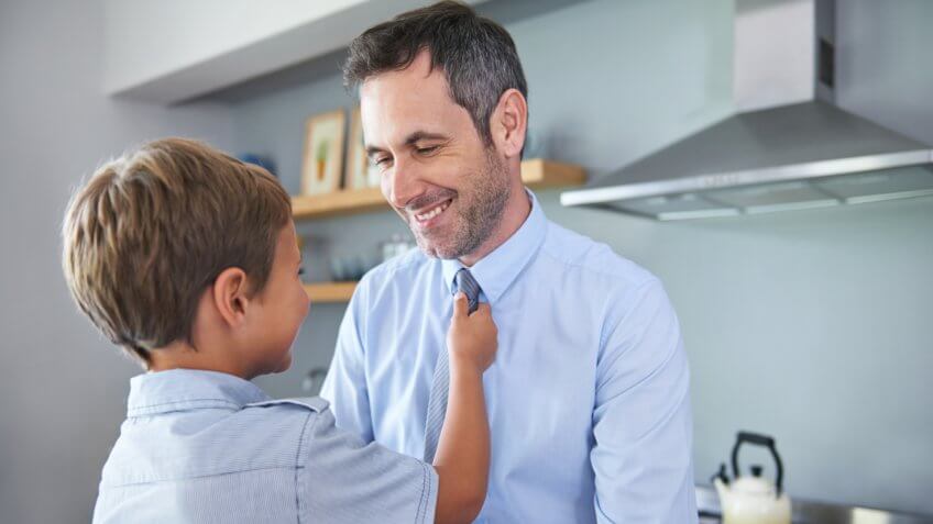 Shot of a little boy adjusting his father's neck tie in the kitchen.