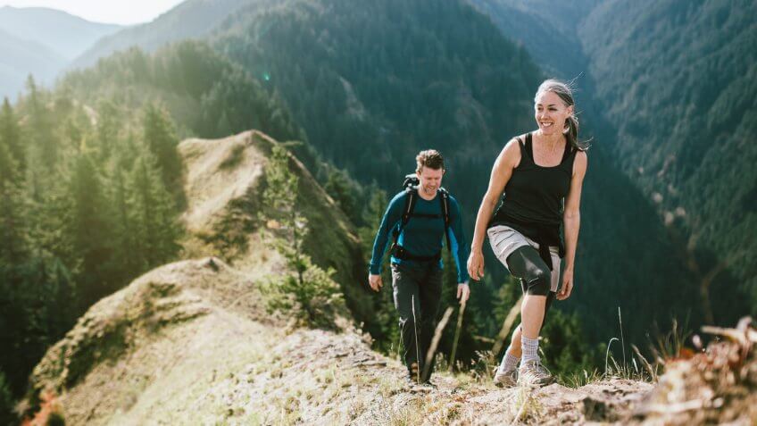 A fit man and woman in their 50's hiking the trail on a mountain ridge, the beautiful Columbia river gorge spreading out behind them.