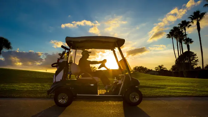 Senior man on golf course driving golf cart at sunrise.