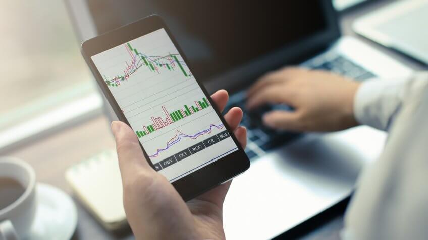 Hand holding smartphone with stock graph, surveying cheap stocks.