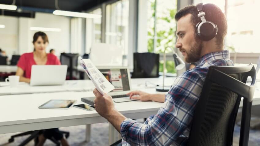Serious man working on laptop while listening to music in open space business company.