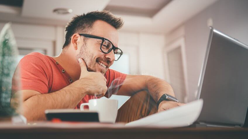 Man in red shirt smiling and using laptop at office.