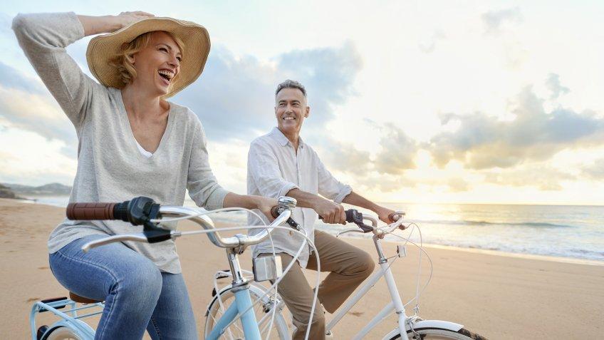 Mature couple cycling on the beach at sunset or sunrise.