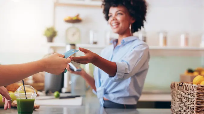 Cropped shot of female employee taking payment from customer, focus on female hands giving credit card for juice bar payment.