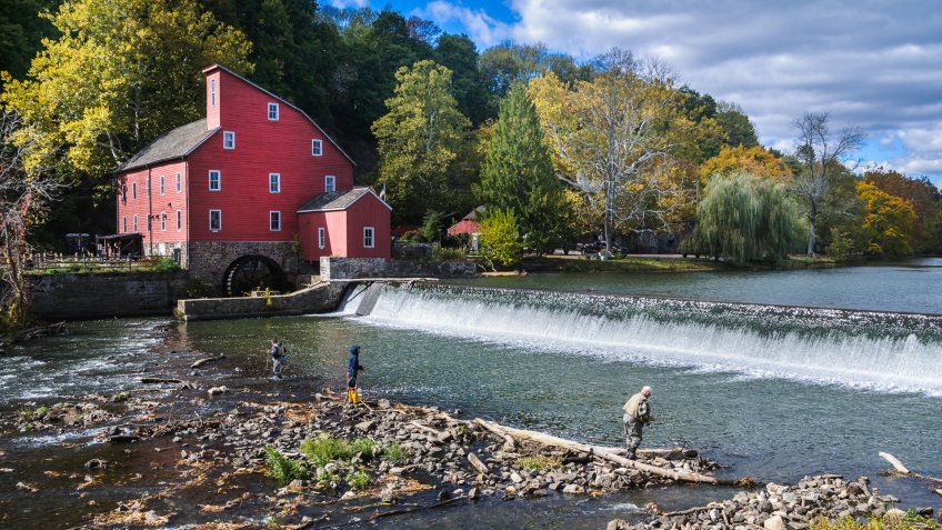 Clinton, New Jersey, USA - October 17, 2015: Three fishermen with rods, nets, and boots fish in the shallow waters below the dam at the Old Red Mill on a crisp Autumn afternoon.