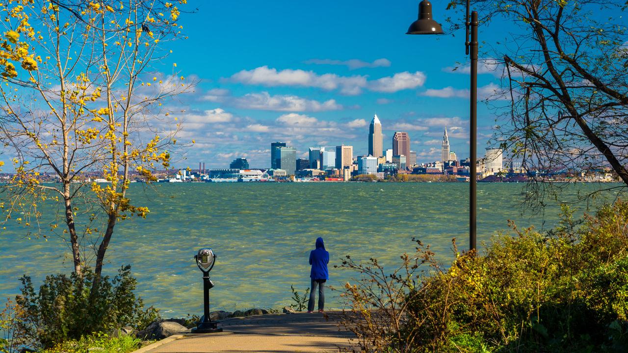 A woman wearing a hood looks at the Cleveland Skyline from a park just beside Lake Erie"n.