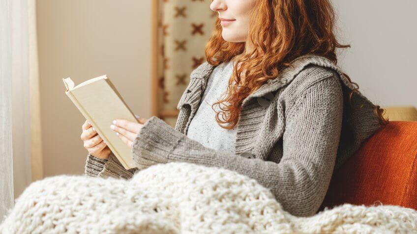 Happy young woman reading a book in a chair.