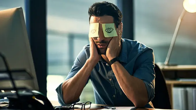 Shot of a tired young businessman working late in an office with adhesive notes covering his eyes.
