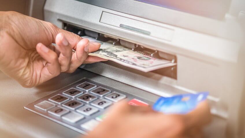 Close up of woman's hand holding dollar banknotes from ATM machine and credit card in the other hand.