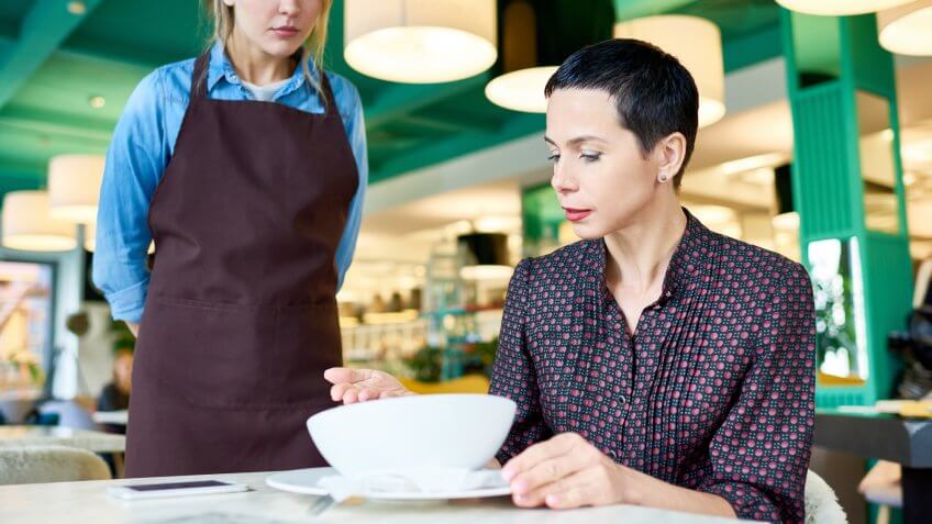 Portrait of elegant woman complaining about food quality and taste to young waitress in cafe.