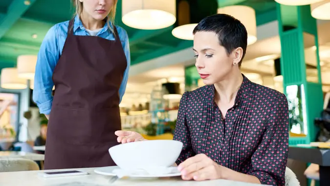 Portrait of elegant woman  complaining about food quality and taste to young waitress in cafe.