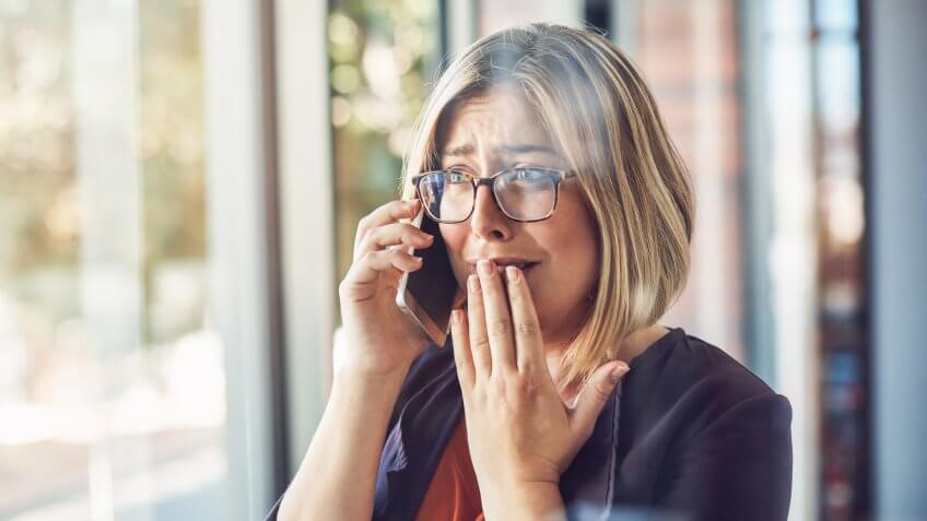 young woman looking stressed while talking on a mobile phone in a modern office.