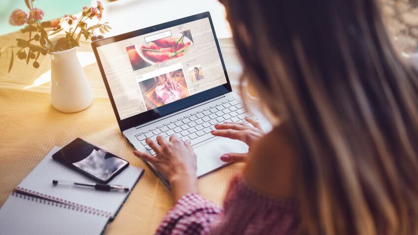 Young food blogger entrepreneur writing blog post and working online on laptop from home office.
