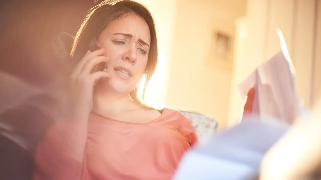 young woman sat on the sofa in her living room is on the phone to her avoiding scams