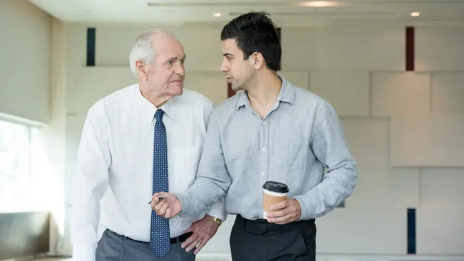Young manager offering pen to upset senior employee for signing document.