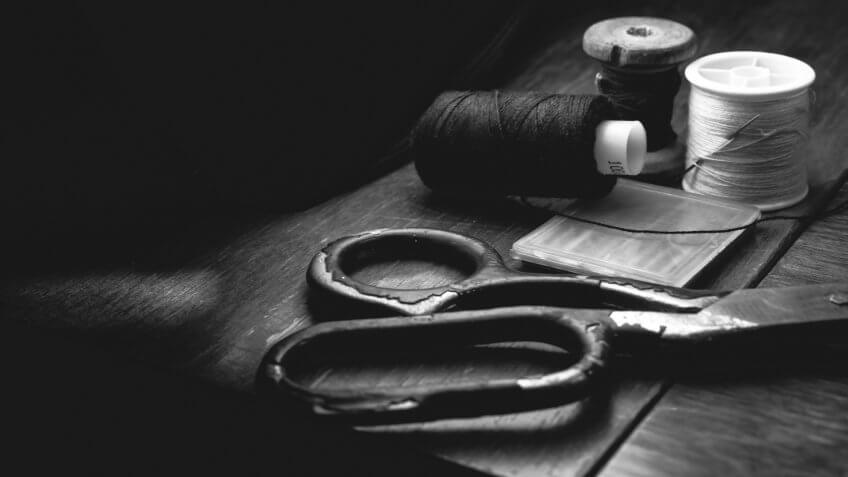 Old sewing machine needle with black thread, on a old grungy work table.