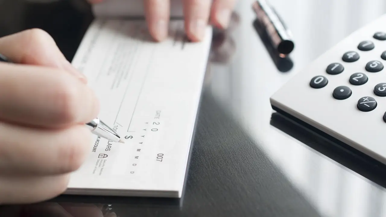 Picture of a person sitting at a desk and holding a pen while writing a check next to a calculator