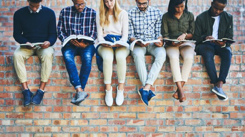 Cropped shot of a group of unrecognizable university students studying while sitting outside on a facebrick wall.