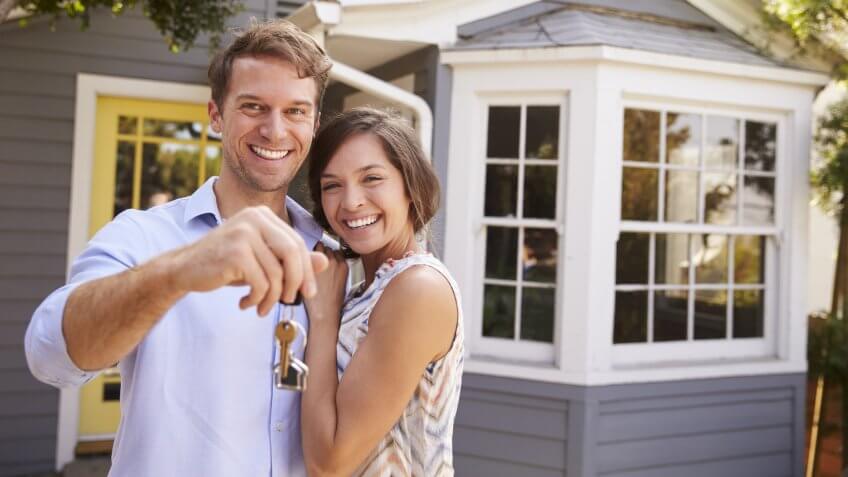 Couple With Keys Standing Outside New Home.