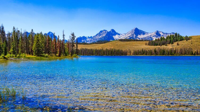 Morning light grazes across the Sawtooth Mountains with lake in foreground - near Stanley, Idaho (ID).