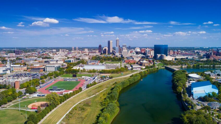 Indianapolis aerial view with Downtown Indianapolis and a blue sky with clouds in the background, and White River and Indiana University - Purdue University Indianapolis(left) and Indianapolis Zoo (right) in the foreground.