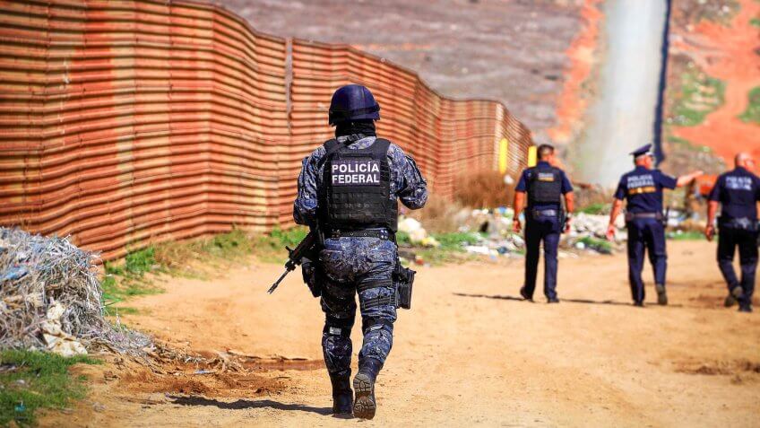 Mexico Federal Police walking along USA Mexico border wall