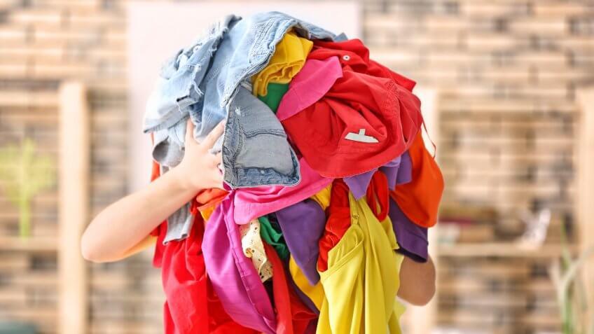 Woman holding pile of colorful clothes indoors.