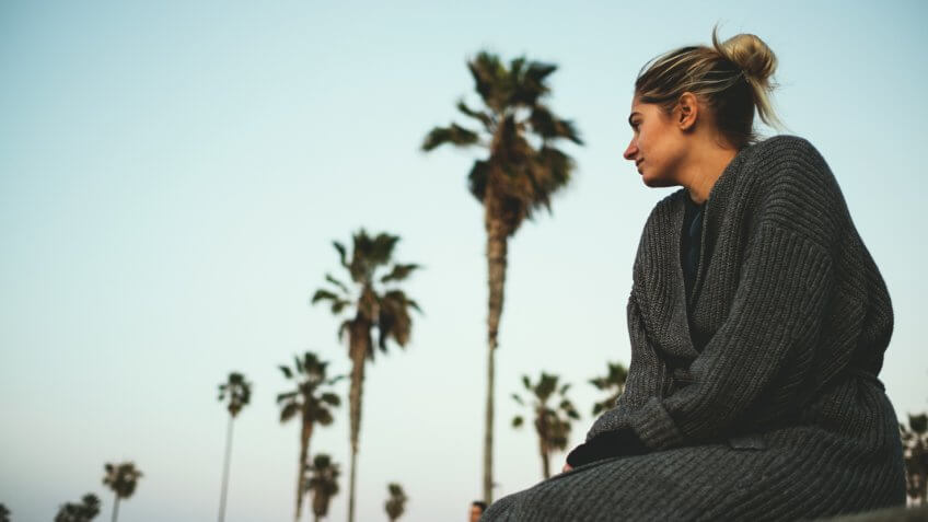Woman sitting on ledge with palm trees in the background