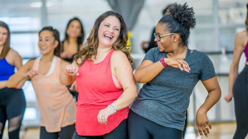 A multi-ethnic group of adult women are dancing in a fitness studio.