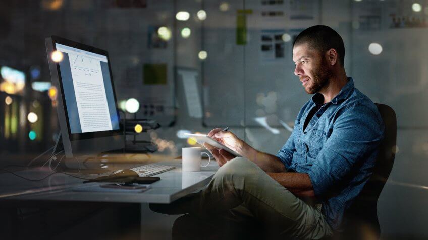 Shot of a businessman using a computer and digital tablet during a late night at the office.
