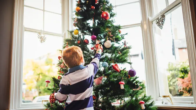A young red head boy is decorating the Christmas tree in his home.