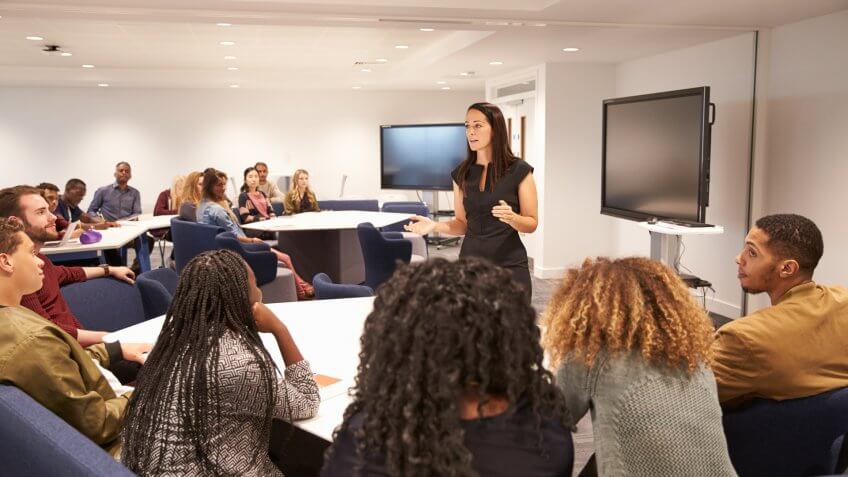 Female teacher addressing university students in a classroom.