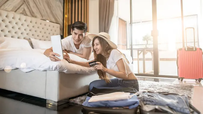 Happy couple packing suitcase on floor in room use tablet for search travel trip online use credit card.