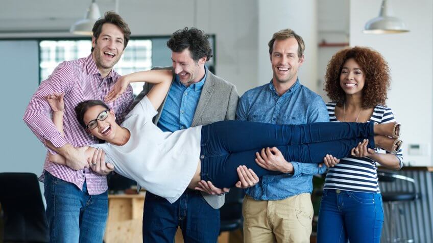 Portrait of a group of smiling coworkers supporting another while having fun in an office.