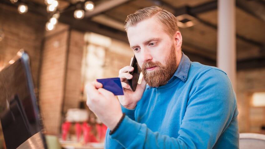 Young, redhead businessman, on coffee break browsing internet, making oline purchase with credit card.