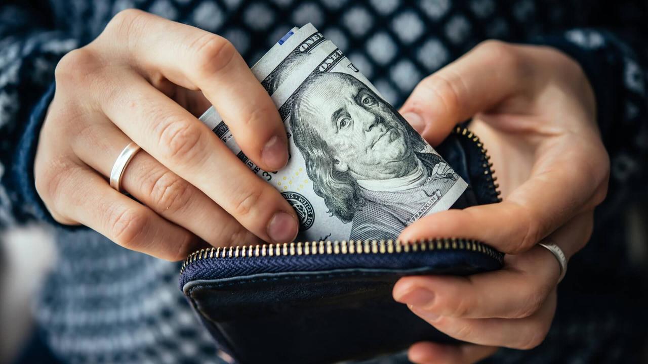 woman putting hundred dollar bills in her purse wallet