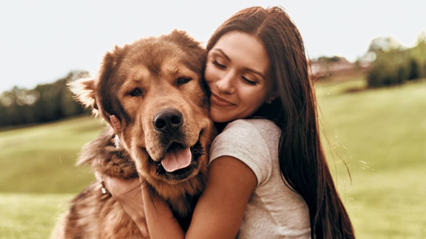 Beautiful young woman keeping eyes closed and smiling while embracing her dog outdoors.