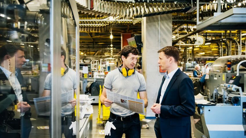 Mechanic and manager talking nearby a machine in a big printery.