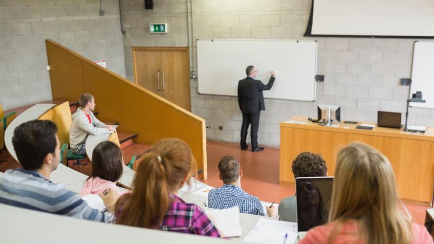 Rear view of a male teacher with students at the college lecture hall.