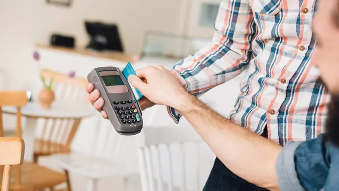 Young man in a coffee shop using his credit card with a credit card reader.