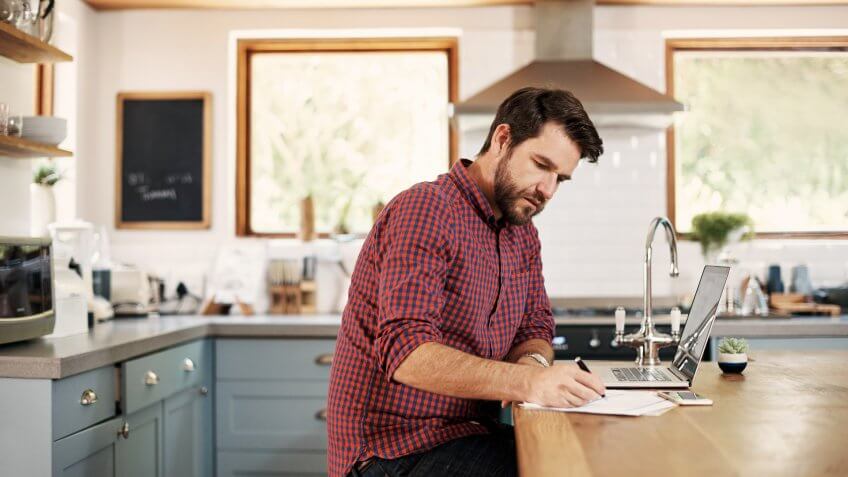 Shot of a handsome man sitting at his kitchen counter with his laptop.