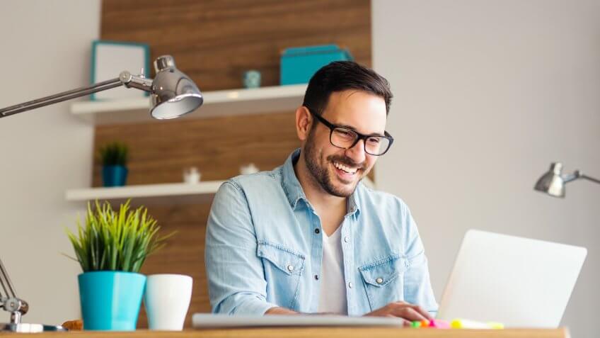 Smiling young freelancer typing on his laptop at the office.