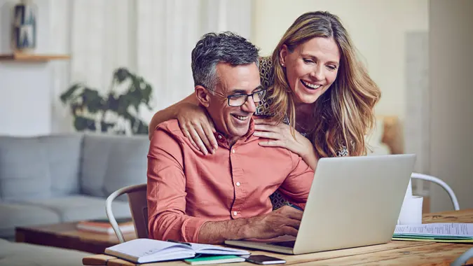 Shot of a mature woman leaning on her husband while he works on his laptop.