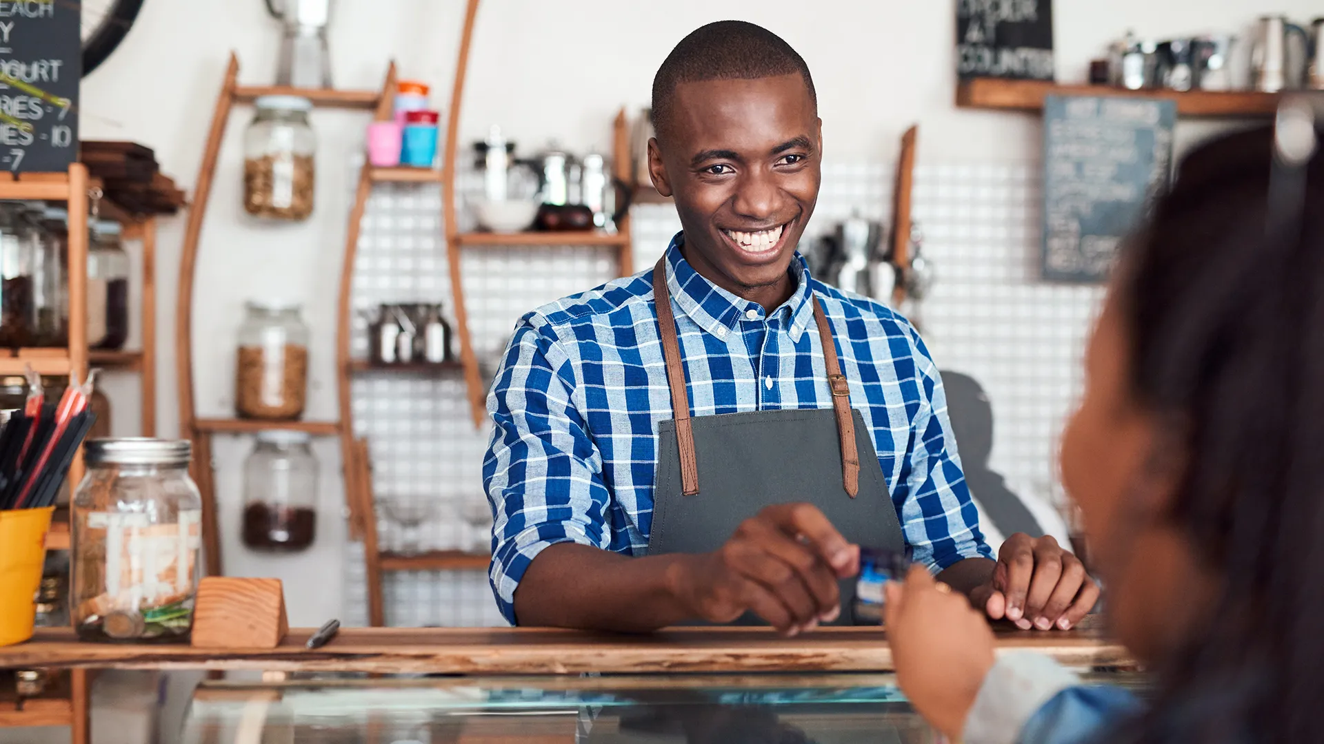 微笑的咖啡师站在咖啡馆的柜台后面，从顾客那里拿信用卡付款-图片。