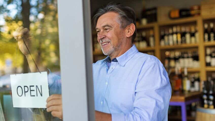 Wine shop owner holding open sign.